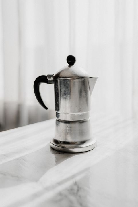 Café-Quality Coffee at Home: The Indian Guide to Espresso, Filter, and Cold Brew 1 A moka pot on a gas stove alongside whole coffee beans and a manual grinder on a kitchen counter