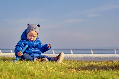 Cute Boy in a Blue Jacket Sitting on the Grass