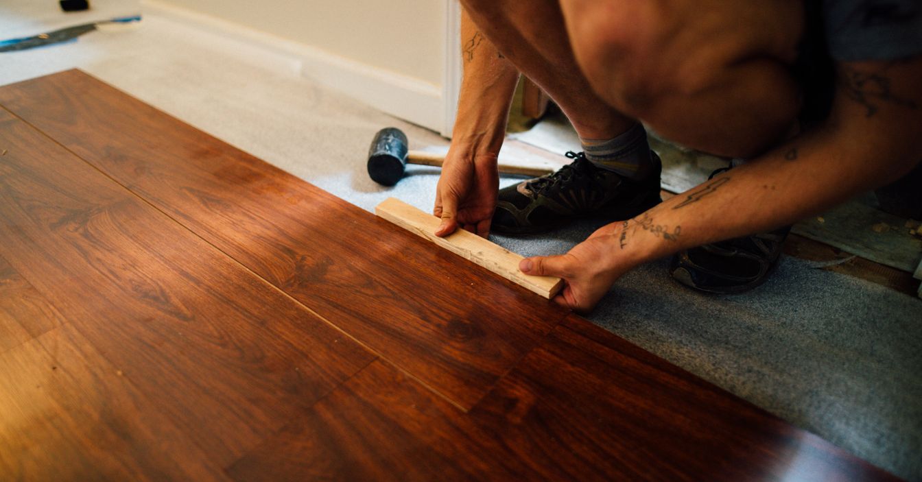 Faceless male master laying wooden laminate flooring using mallet in apartment during renovation