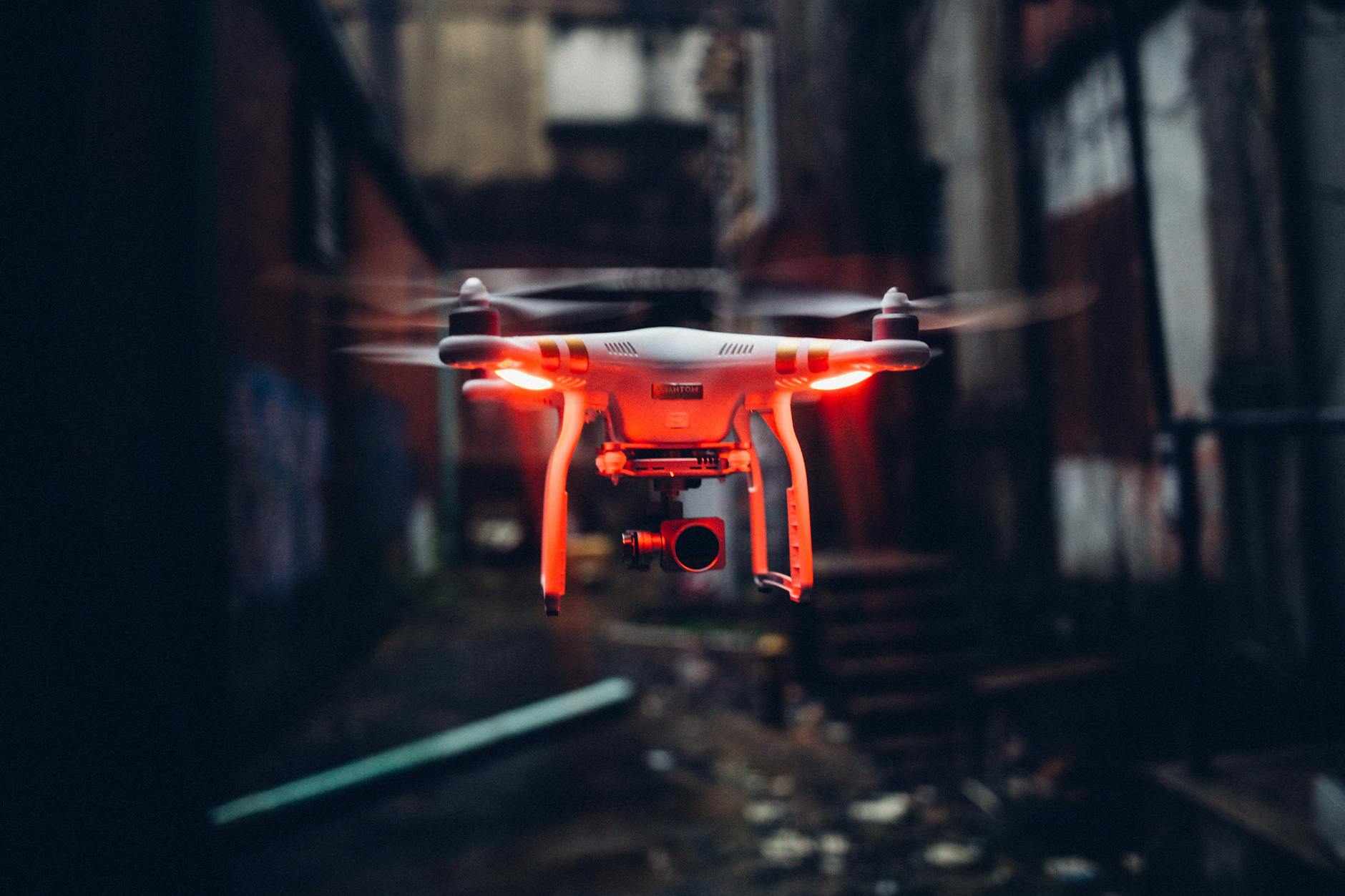 Red glowing modern drone flying in air on blurred background of gloomy industrial street