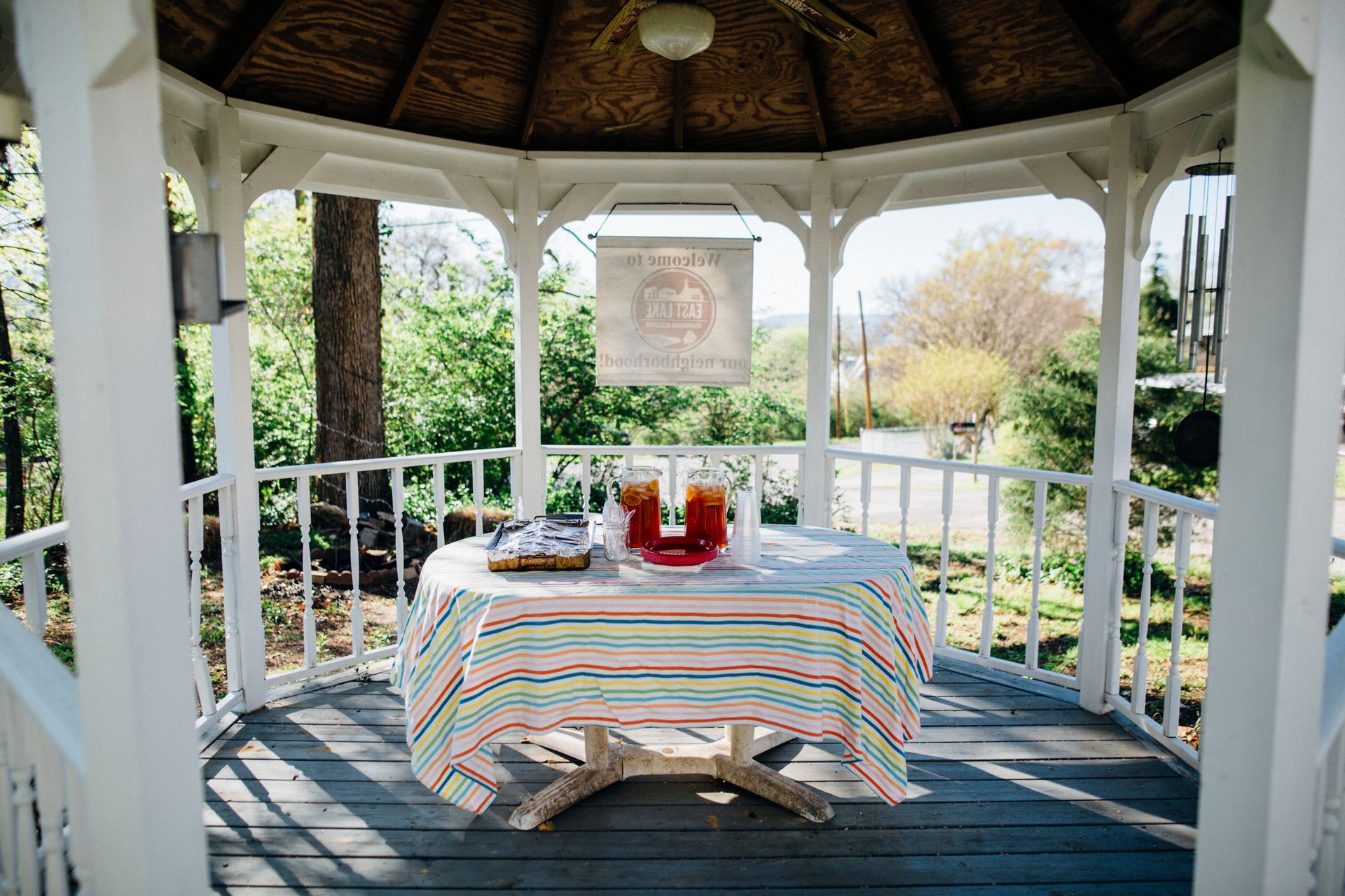 Gazebo with a table set for an outdoor gathering, featuring drinks and snacks in a natural garden setting.