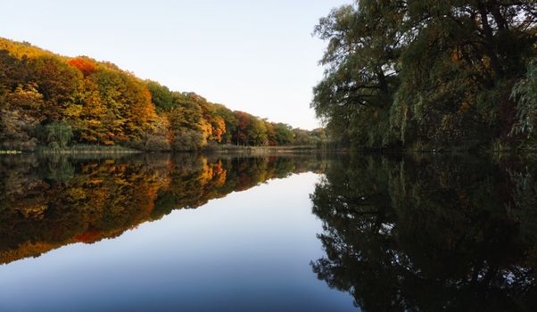A tranquil lake with autumn foliage reflecting in calm water, creating a peaceful landscape.