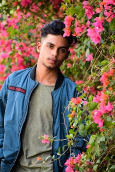 一个年轻人自信地站在郁郁葱葱的户外环境中，身旁是五颜六色的粉红色九重葛