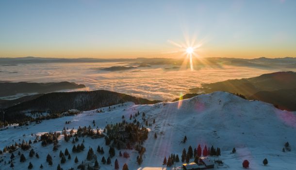 Aerial view of snowy hills covered with green trees and clouds during dawn