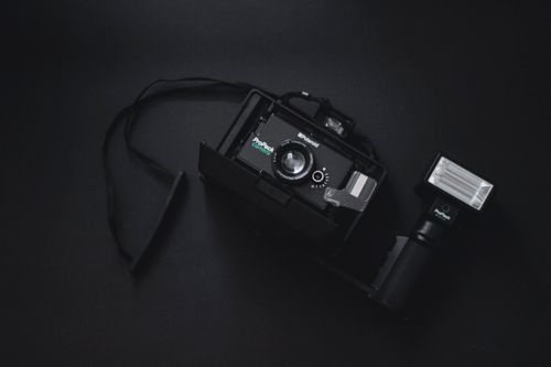 Free A classic Polaroid camera with detachable flash on a dark background, showcasing vintage photography equipment. Stock Photo
