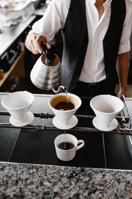 Barista pouring hot coffee using a kettle into a cup in a modern indoor coffee shop.