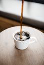 将热气腾腾的黑咖啡倒入木桌上的白色陶瓷杯里
