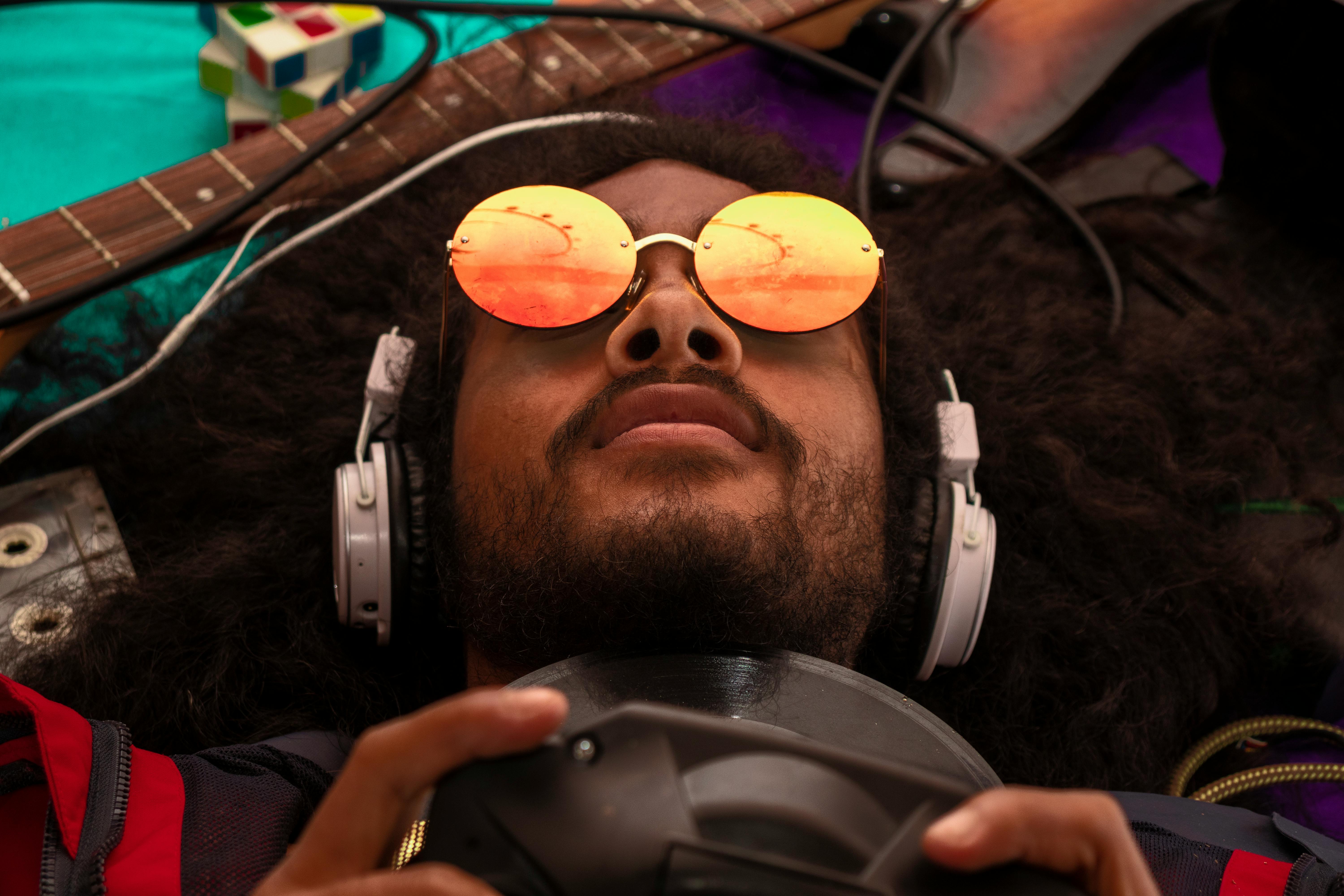 Close-up of a young man with headphones and sunglasses lying next to a guitar.