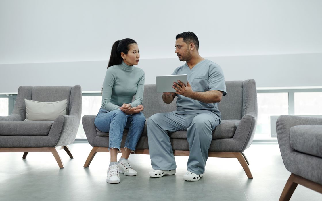 Healthcare professional in scrubs explaining information on a tablet to a seated patient
