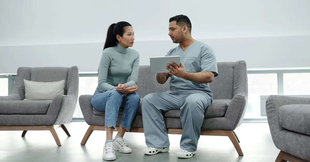 A doctor and a patient sitting on a sofa looking at a tablet, representing FDA AI medical device SaMD compliance 2026