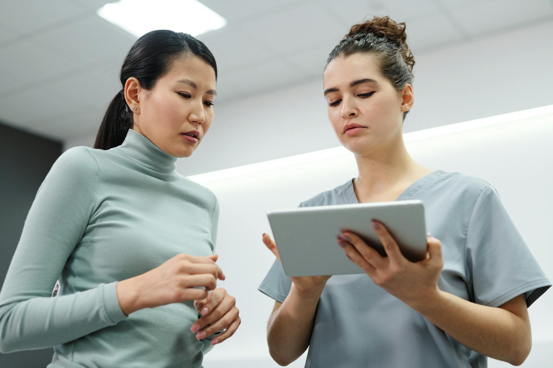 Two women engaged in a healthcare consultation using a digital tablet indoors.