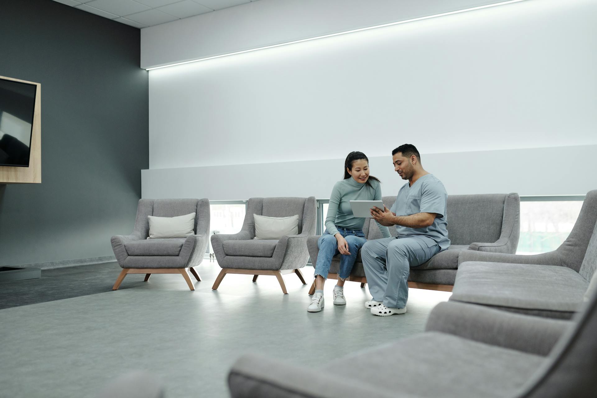 A doctor in scrubs consulting with a patient in a modern, indoor waiting area.