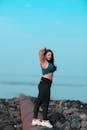 Ethnic woman standing with hands behind head on stony beach