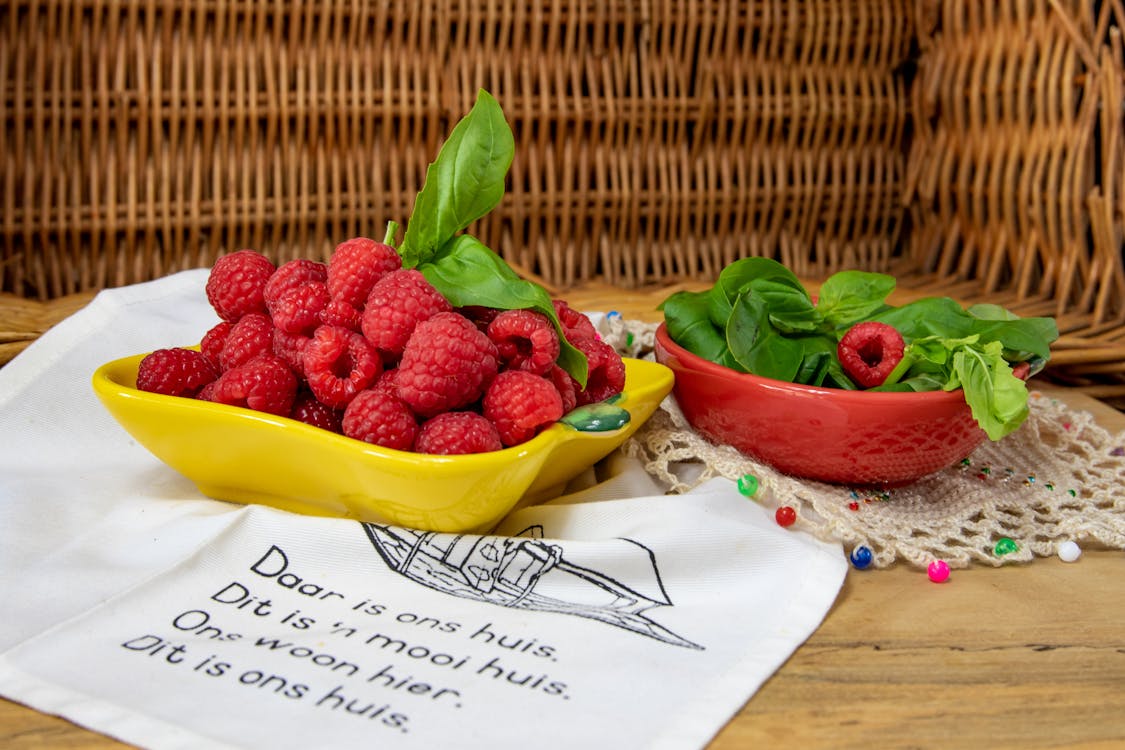 Red Raspberries Beside a Bowl of Basil Leaves