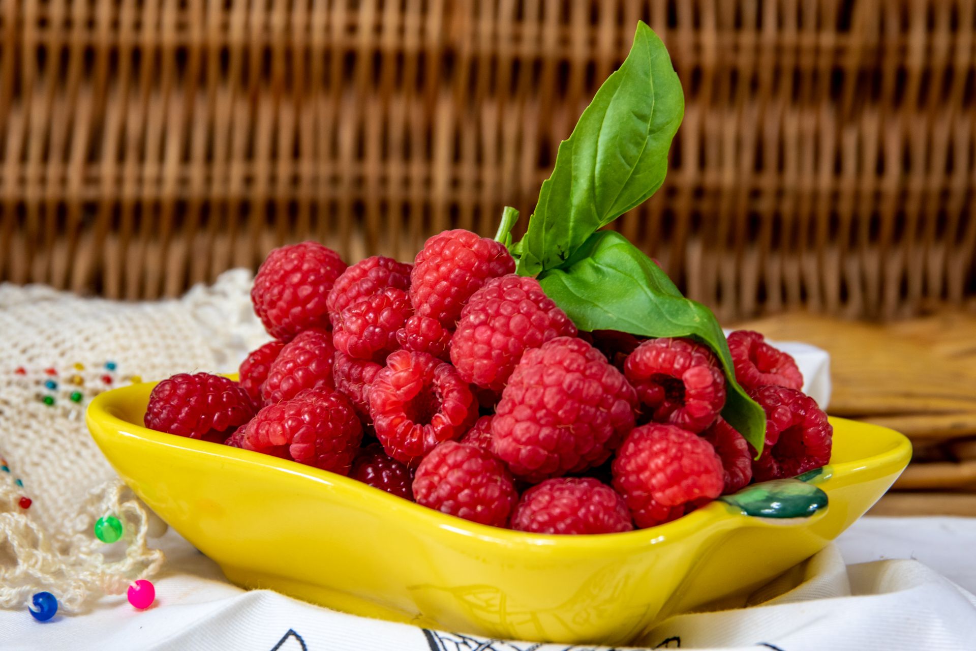 Vibrant raspberries with fresh basil in a yellow dish, perfect for healthy snacking.