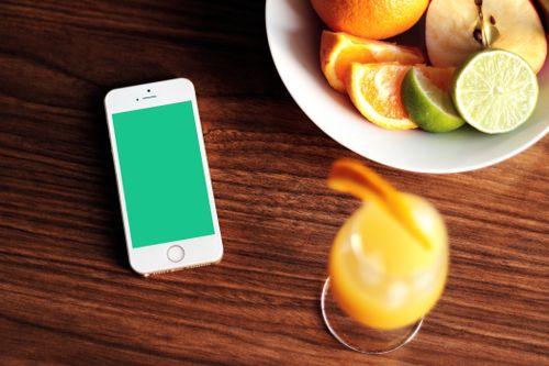 Free Mockup of a smartphone with fresh citrus fruits and juice on a wooden table. Stock Photo
