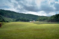 宁静的乡村景观中，绿色的山丘环绕着一座小小的屋舍，天空多云