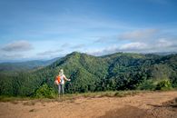 Back view of unrecognizable female hiker in casual clothes with backpack and trekking pole recreating and admiring amazing mountain view on sunny day