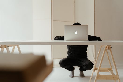 A person working in a minimalistic home office setup with a laptop on a white table.