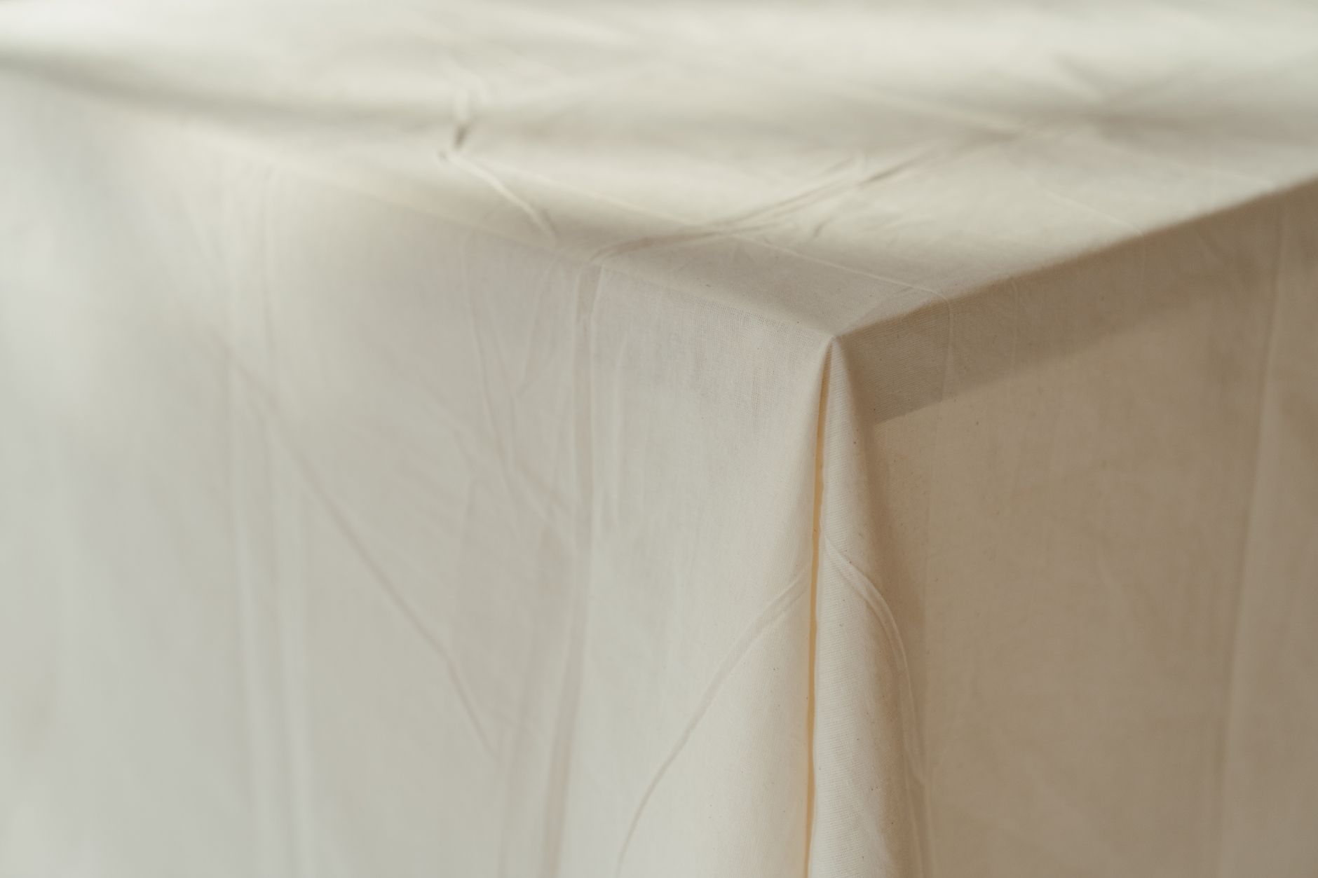 A close-up of a beige tablecloth draped over a table, showcasing texture and folds.