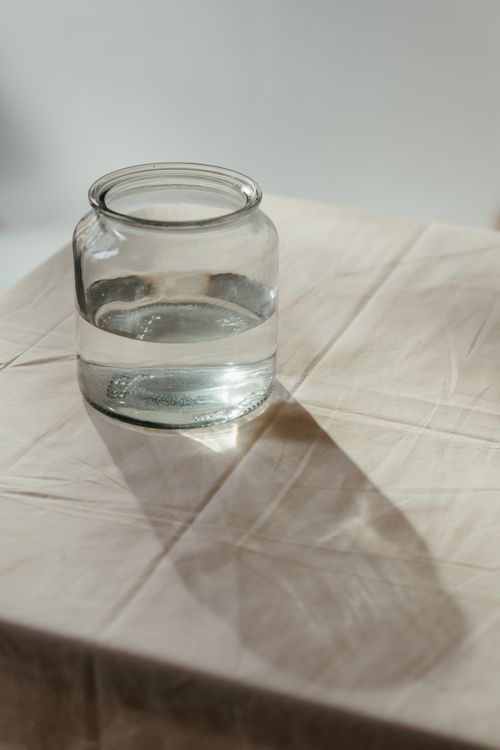 Free A transparent glass jar casting a shadow on a sunlit table with a simple tablecloth. Stock Photo