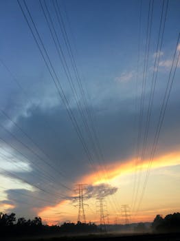 Silhouetted power lines stretch into the dramatic sunset sky, showcasing energy and nature's beauty.