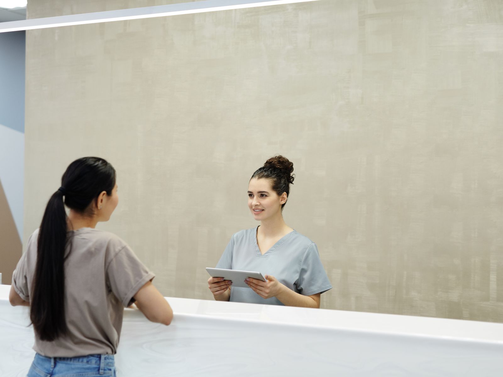 Smiling receptionist using a tablet while helping a patient at a reception desk
