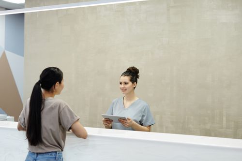 Free A smiling receptionist with a tablet assists a patient at a medical facility reception desk. Stock Photo