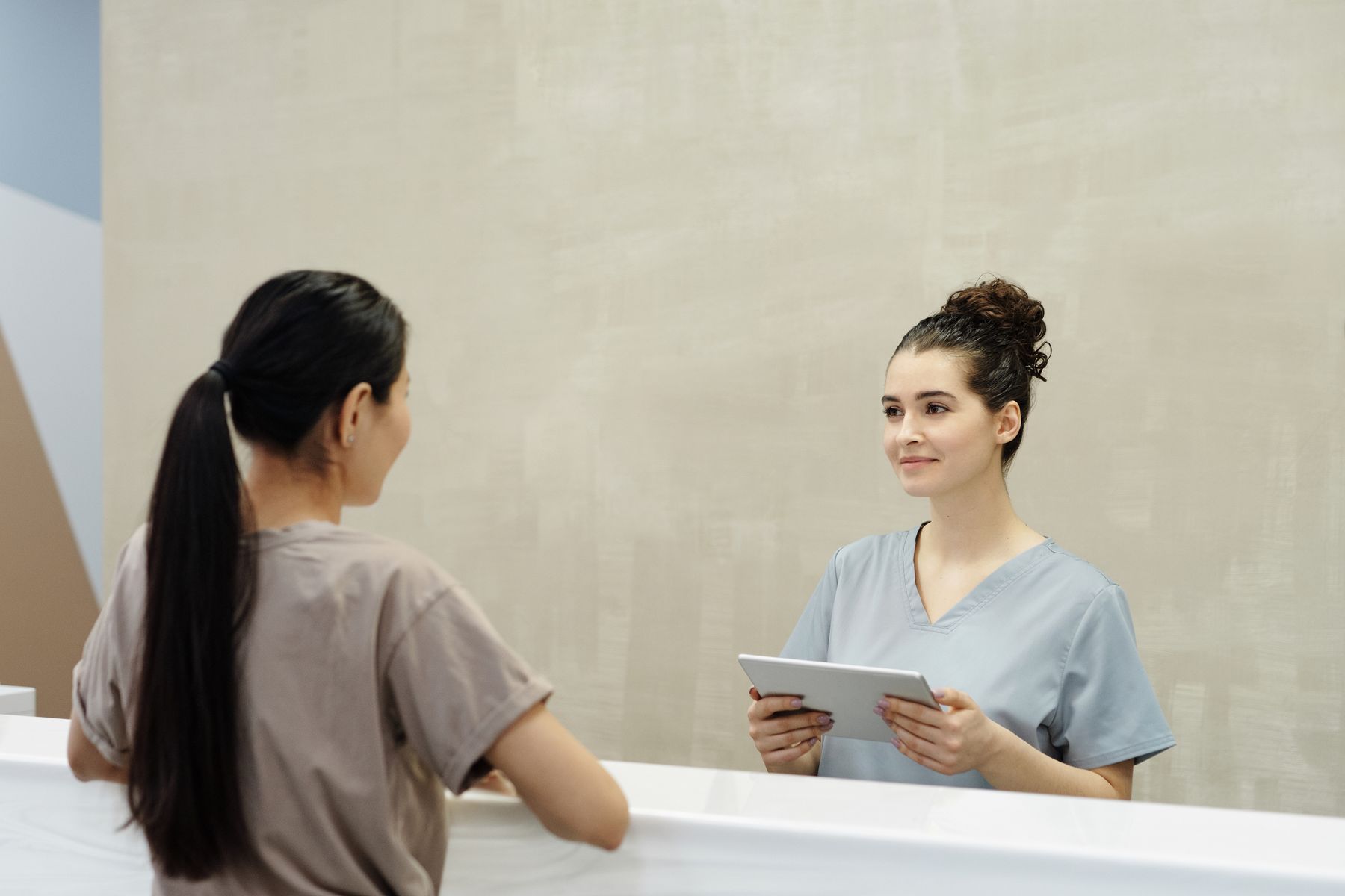 Receptionist using a tablet while assisting a patient at a modern front desk