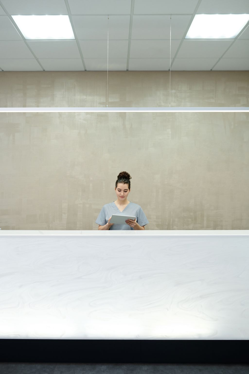 One member of staff alone behind a long clinic reception counter