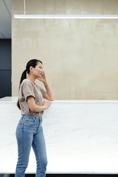 一位年轻女子若有所思地倚在办公桌旁，室内环境休闲而现代