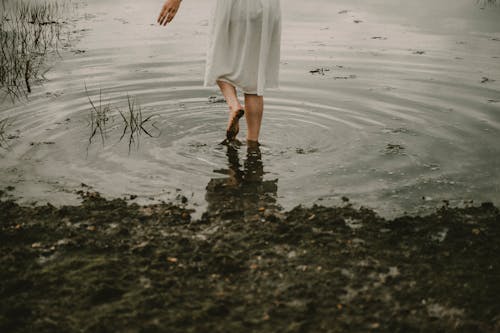 Unrecognizable woman walking alone in dirty pond on cloudy day