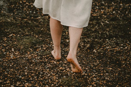 Free From above of crop anonymous barefooted lady in casual white dress walking alone on wet stony beach Stock Photo