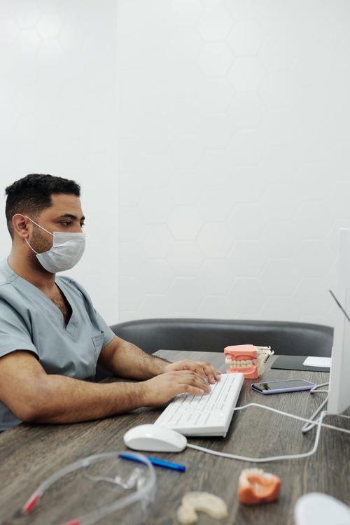 Free A dentist wearing a face mask types on a computer in a clinic setting. Stock Photo