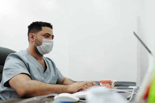 医疗专业人员在诊所办公室的电脑前工作，他们穿着手术服、戴着口罩
