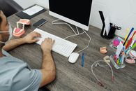 牙医坐在办公桌前，对着电脑打字，周围摆着牙齿模型和工具