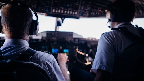 Free Back view of anonymous male pilots in uniform and headset navigating modern airplane while taking off Stock Photo