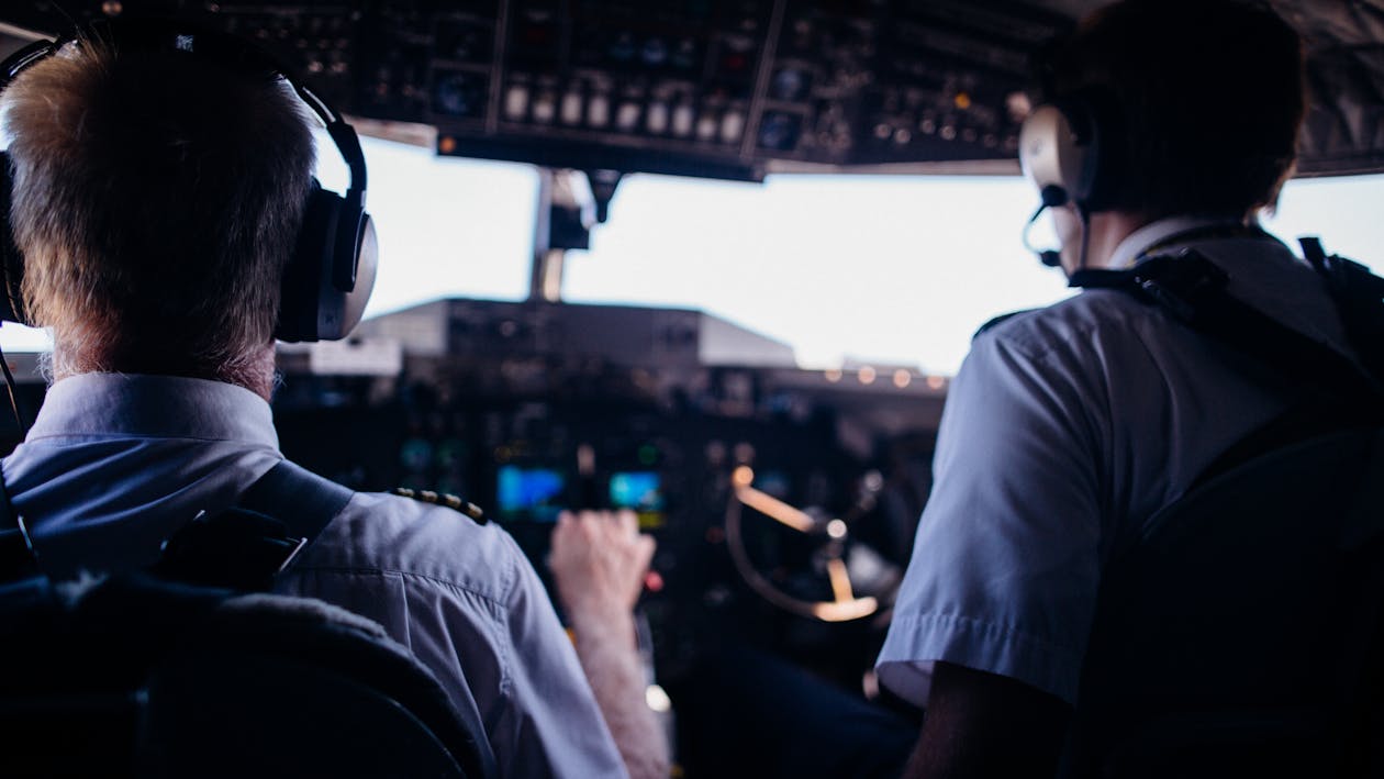 Free Back view of anonymous male pilots in uniform and headset navigating modern airplane while taking off Stock Photo