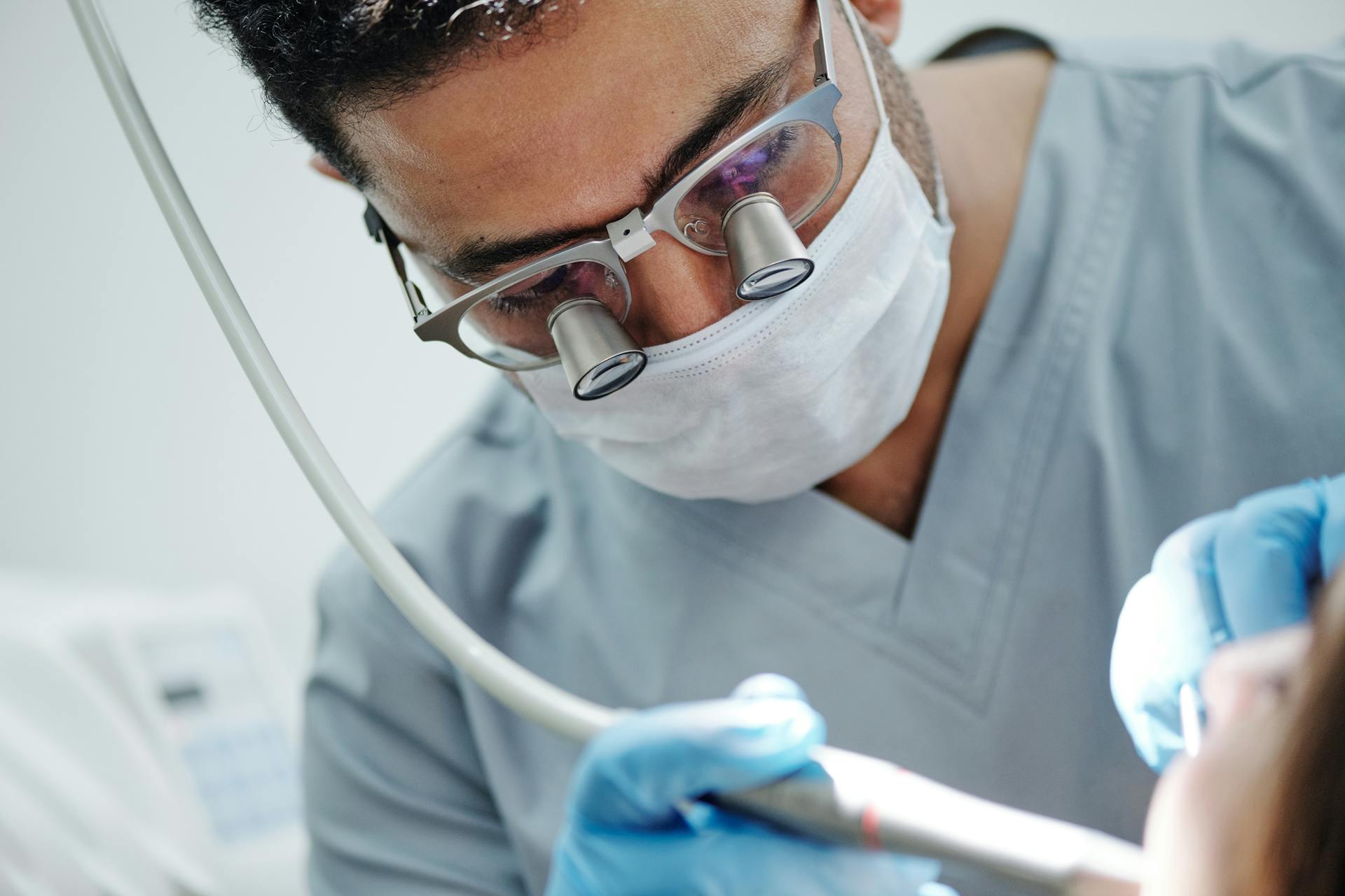 Man in Gray Scrub Suit Wearing a Pair of Dental Loupe