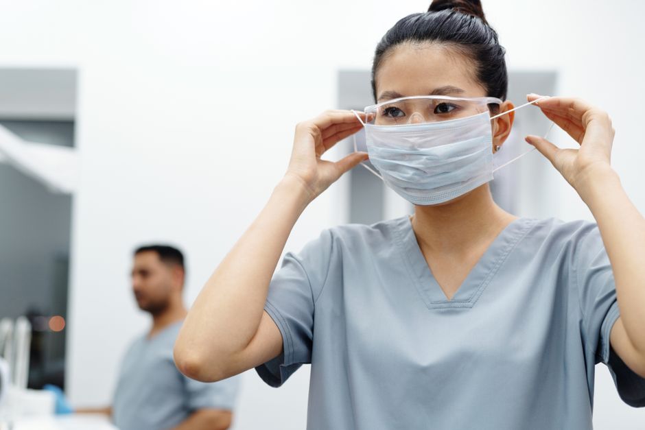 Asian female healthcare worker adjusts protective mask and goggles in a medical setting.