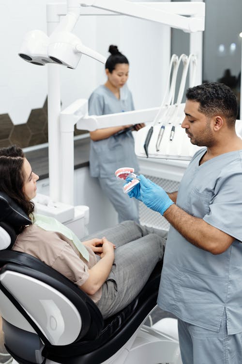 Free A Man in Gray Scrub Suit Standing Beside a Woman on the Dental Chair Stock Photo