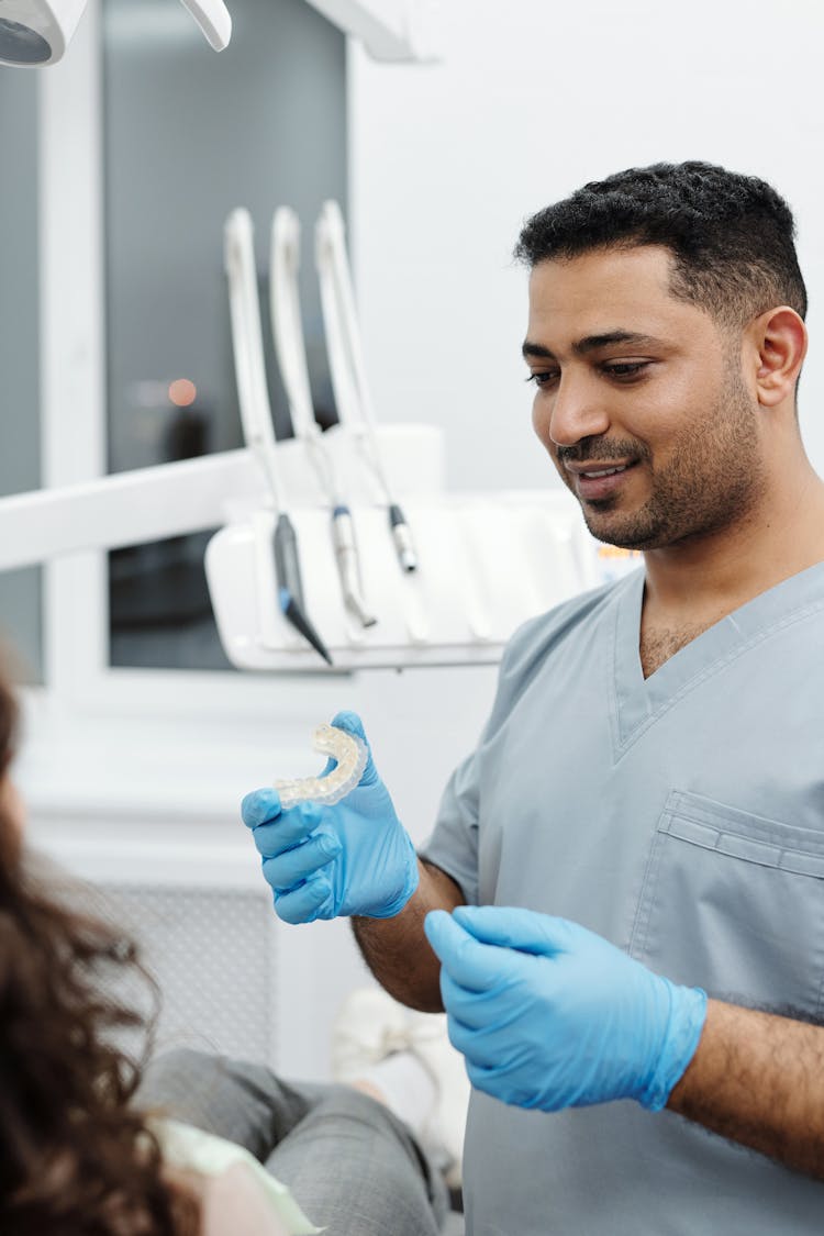 A Man In Scrub Suit Holding A Ceramic Teeth