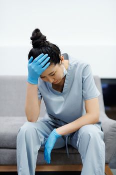 一名穿着手术服的女医护人员疲惫不堪地坐在沙发上，手托着头，看起来很紧张