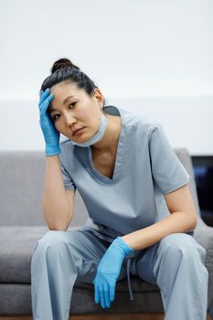 护士疲惫不堪，穿着蓝色工作服，手放在头上休息
