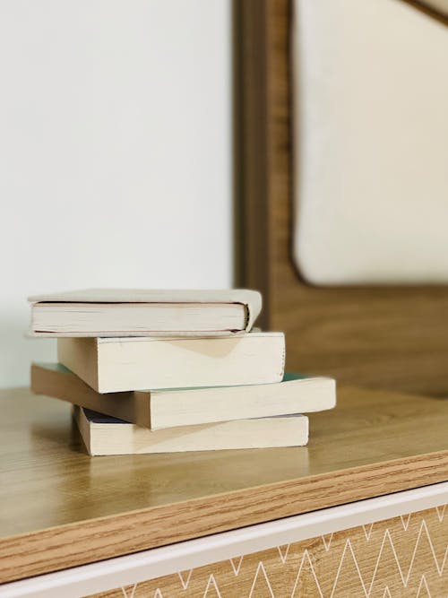Free Stack of various books placed on wooden nightstand near bed in cozy light room Stock Photo