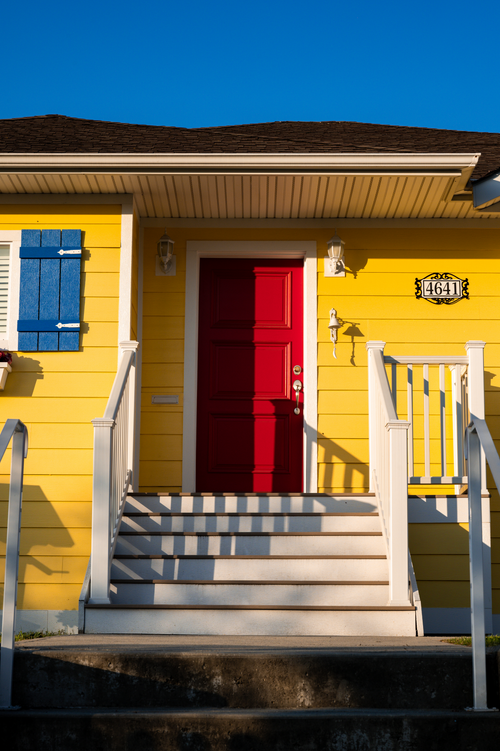 Free Colorful house exterior featuring yellow walls and a striking red door. Stock Photo