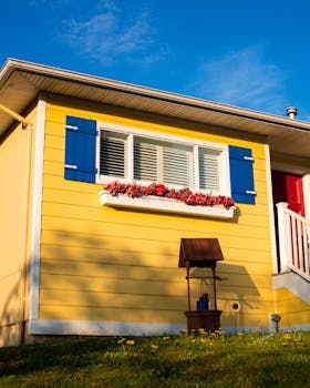 Bright yellow house exterior with blue shutters and vibrant flower box on a sunny day.