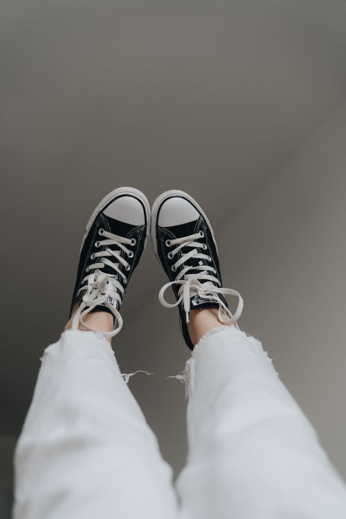 Free Elevated view of black sneakers worn with white denim jeans for a casual look. Stock Photo