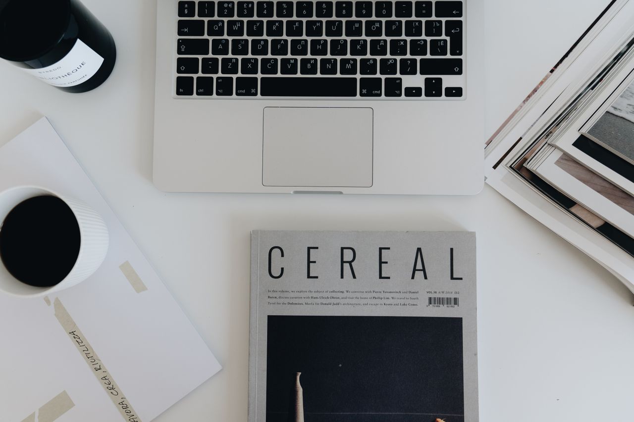 Minimalist workspace showing a laptop, magazines, and coffee on a desk