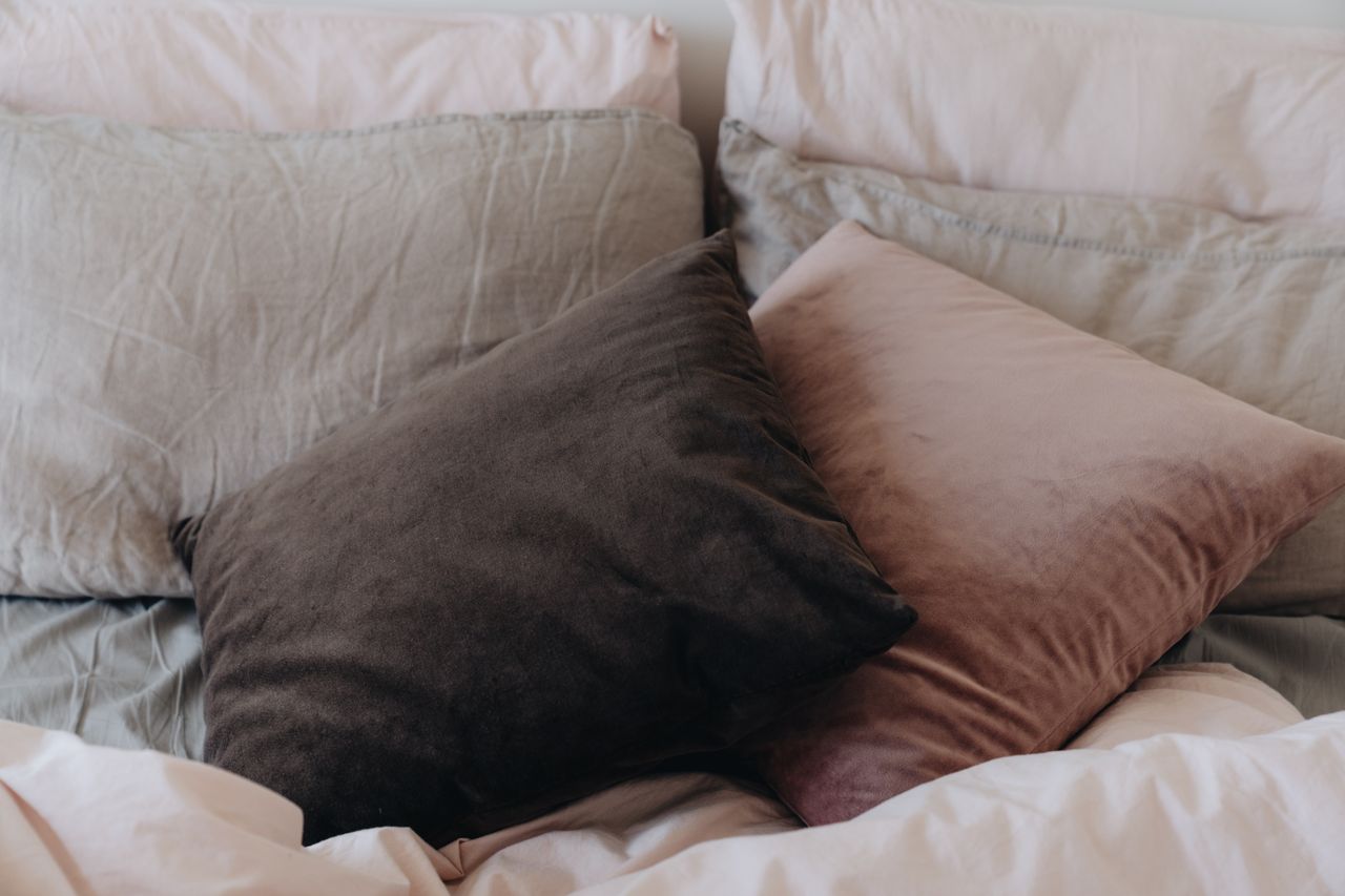 Layered bed pillows with linen shams at the back and velvet cushions in front on a neatly made bed